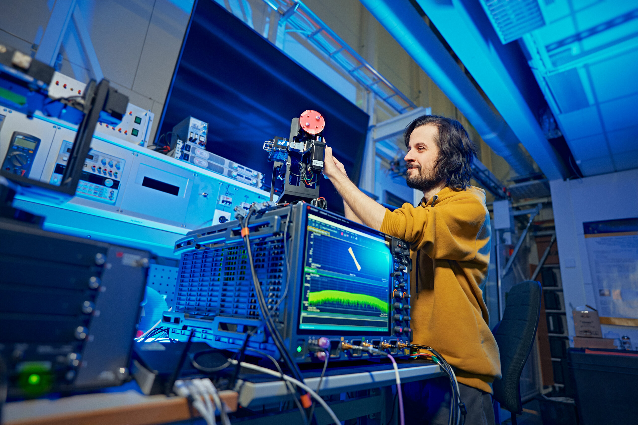 A researcher in a laboratory adjusting radio frequency equipment with signal analysis on a monitor, studying 6G wireless propagation.