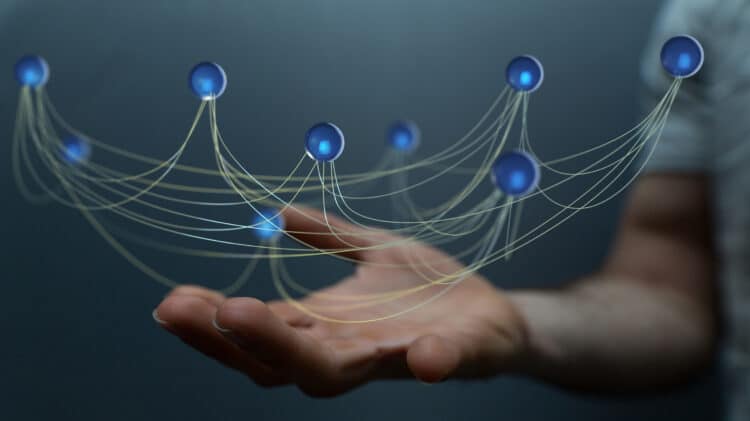 A hand supporting a network of interconnected blue nodes with glowing centers. Thin lines connect the nodes, symbolizing data flow and digital connectivity, representing the concept of 6G-powered IoT networks.