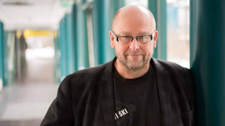 Professor Ari Pouttu, Vice Director of 6G Flagship, standing in a corridor with teal pillars.