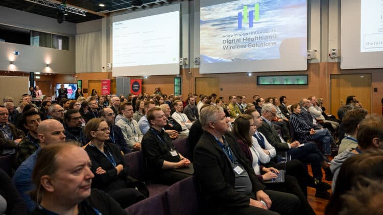 Audience at the Nordic Conference on Digital Health and Wireless Solutions attentively listening to a presentation, with the event agenda displayed on the screen.