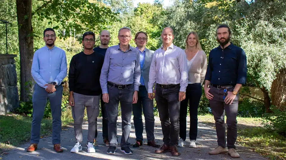 A group of eight researchers and professionals from the IMMERSE project posing outdoors, surrounded by greenery, during their team meeting in Sundsvall, Sweden.