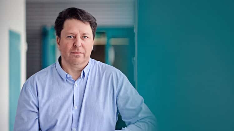 Professor Matti Latva-aho standing in a University of Oulu's corridore wearing a light blue shirt.